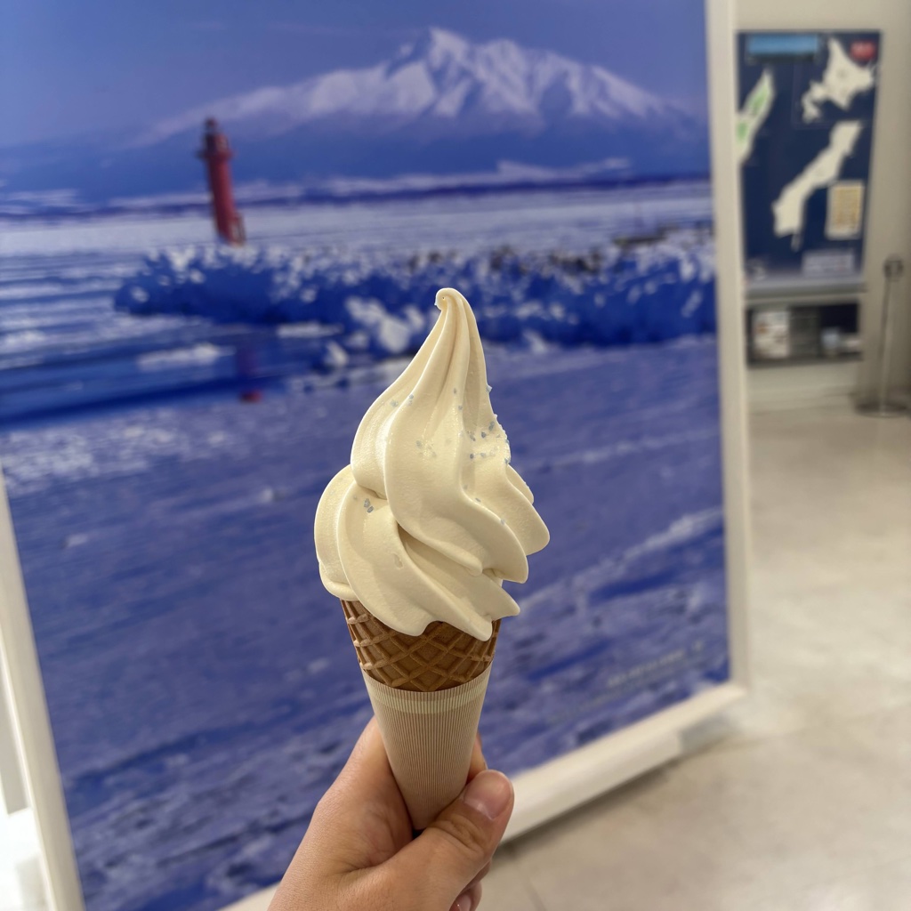 流氷館の売店で味わえる塩ソフト — 背景は流氷の写真パネル