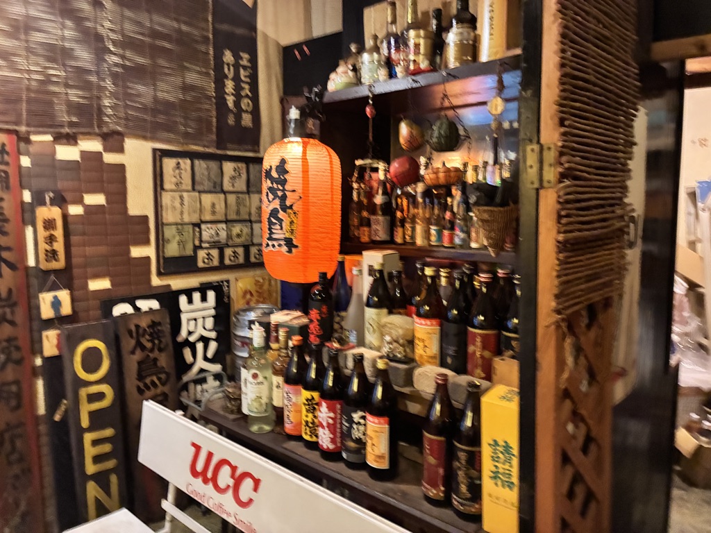居酒屋のカウンター、日本酒瓶が並ぶ賑やかな夜の雰囲気