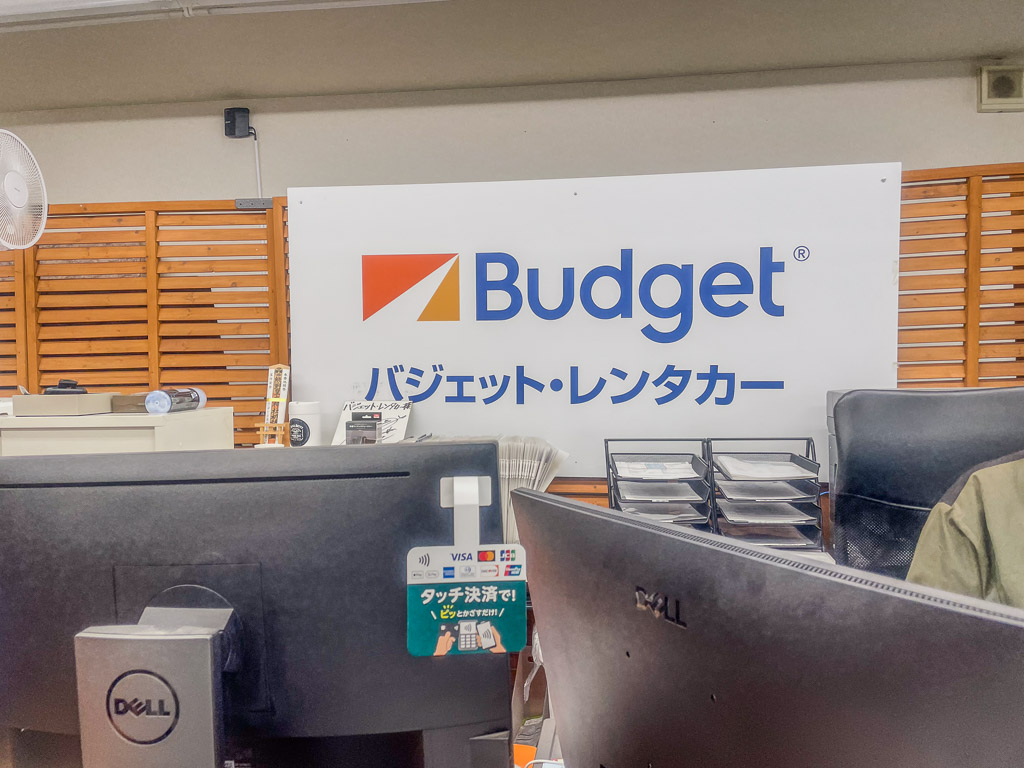 長野レンタカー(バジェット軽井沢駅前店)のカウンターとブランドロゴ>

<p>受け取り店舗は<strong>バジェット・レンタカー 軽井沢駅前店</strong>。<b>軽井沢駅北口から徒歩約5分</b>と、新幹線を降りてキャリーバッグを転がしてもストレスなく歩ける距離です。店の前は静かな路地で、迷うこともありませんでした。</p>

<center><iframe style=