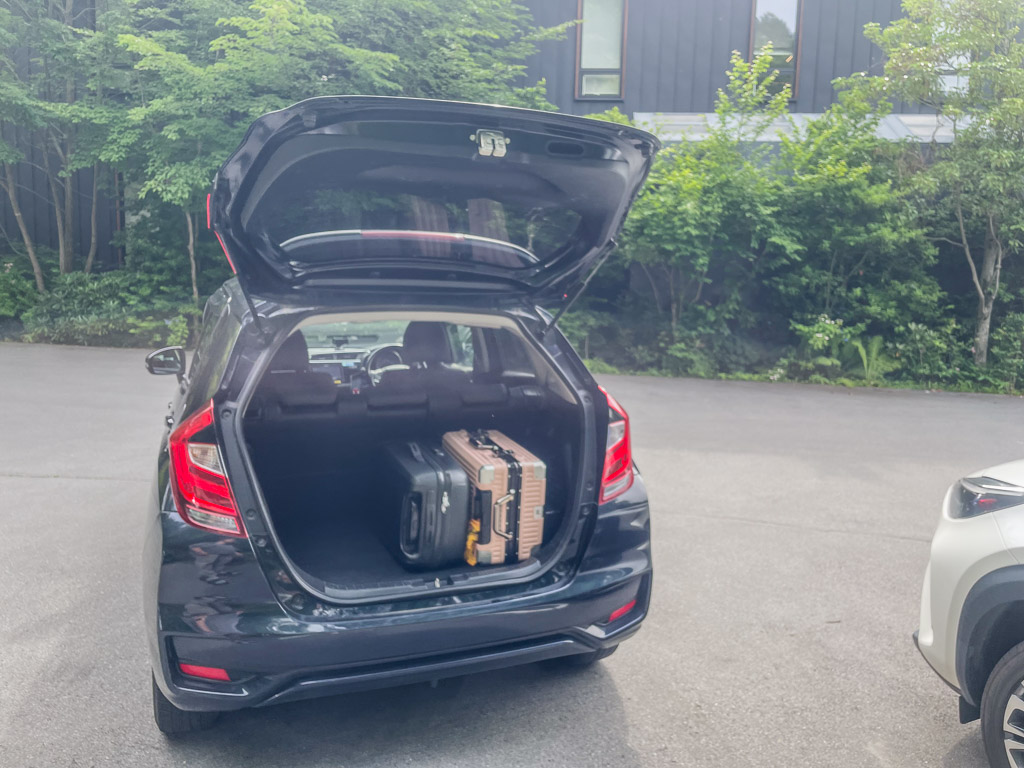 宿の駐車場でホンダ FIT のバックドアを開けスーツケースを積む様子