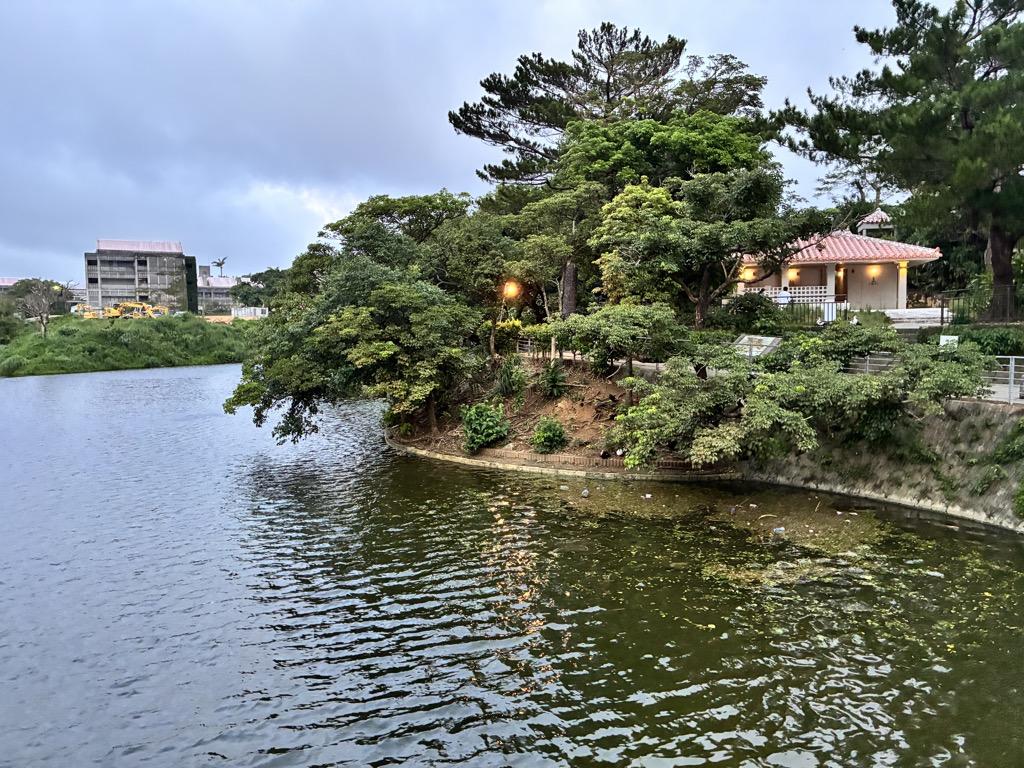 夕暮れに灯りがともる赤瓦の建物と首里城公園の池