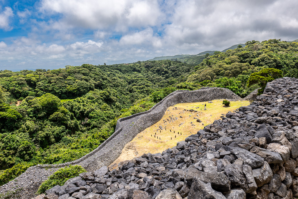 今帰仁城跡の草原と円形建物遺構、背後に石垣と山
