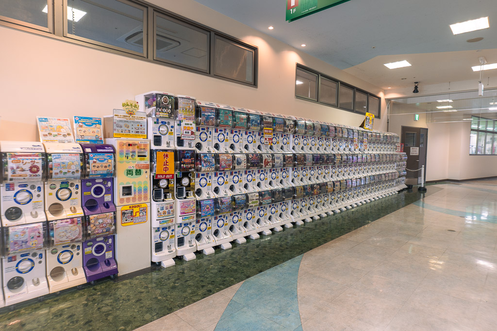 出口付近の巨大ガチャガチャコーナー — 100台以上のカプセルトイマシンが壁面いっぱいに並ぶ