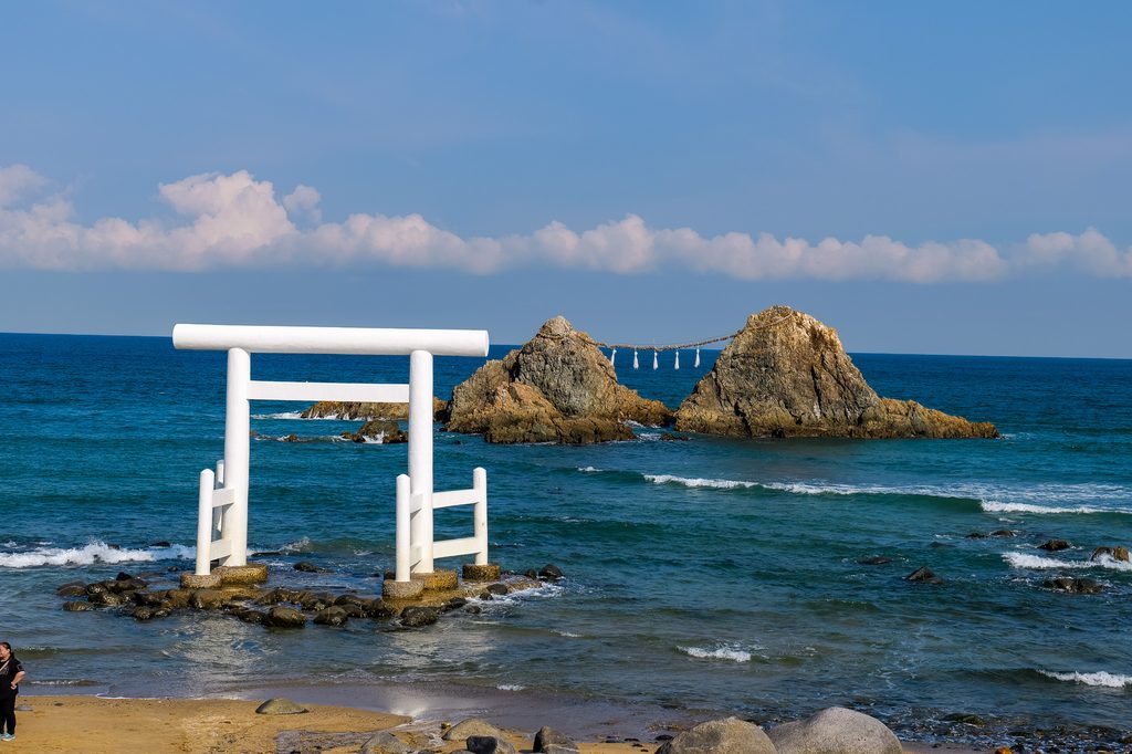 白い鳥居越しに見る夫婦岩のクローズアップ。男岩と女岩、注連縄がはっきり見える構図で、神秘的な雰囲気を強調